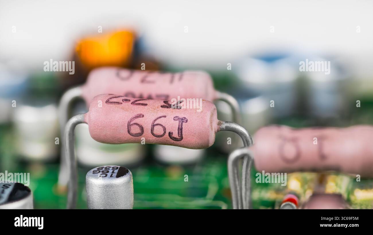 Vue latérale des résistances roses et des condensateurs blancs sur un circuit imprimé vert. Gros plan sur divers composants électroniques sur fond flou de carte de circuit imprimé. Banque D'Images