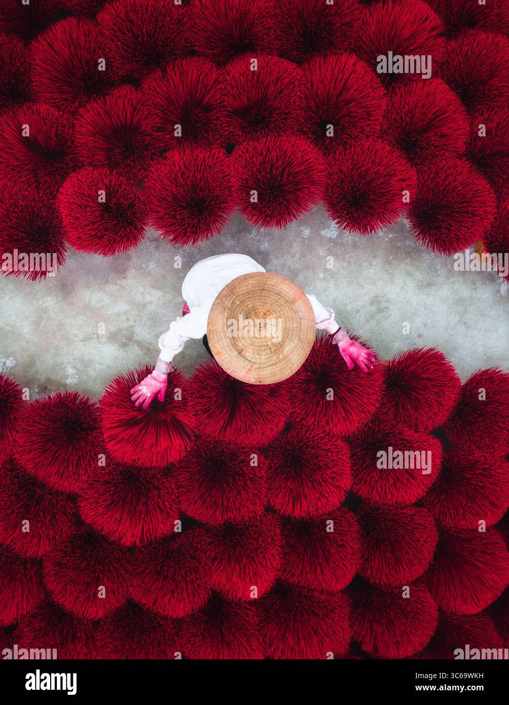 Vue aérienne d'un ouvrier au milieu d'une mer de bâtons d'encens rouges vibrants, créant un contraste visuel saisissant contre le chemin neutre, Quang Phu Cau, Hanoi, Vietnam. Banque D'Images