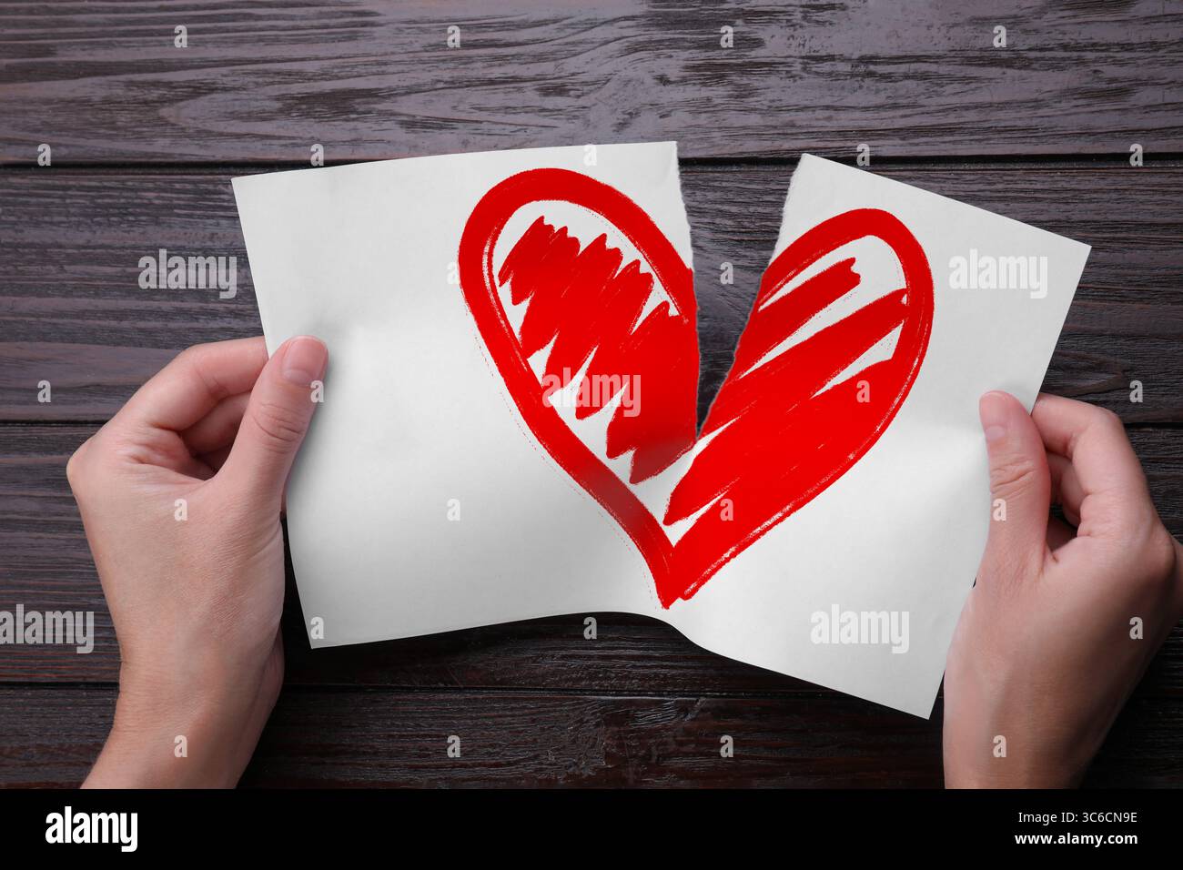 Trahison. Femme déchirant la feuille de papier avec le coeur rouge en moitiés sur fond de bois, gros plan Banque D'Images