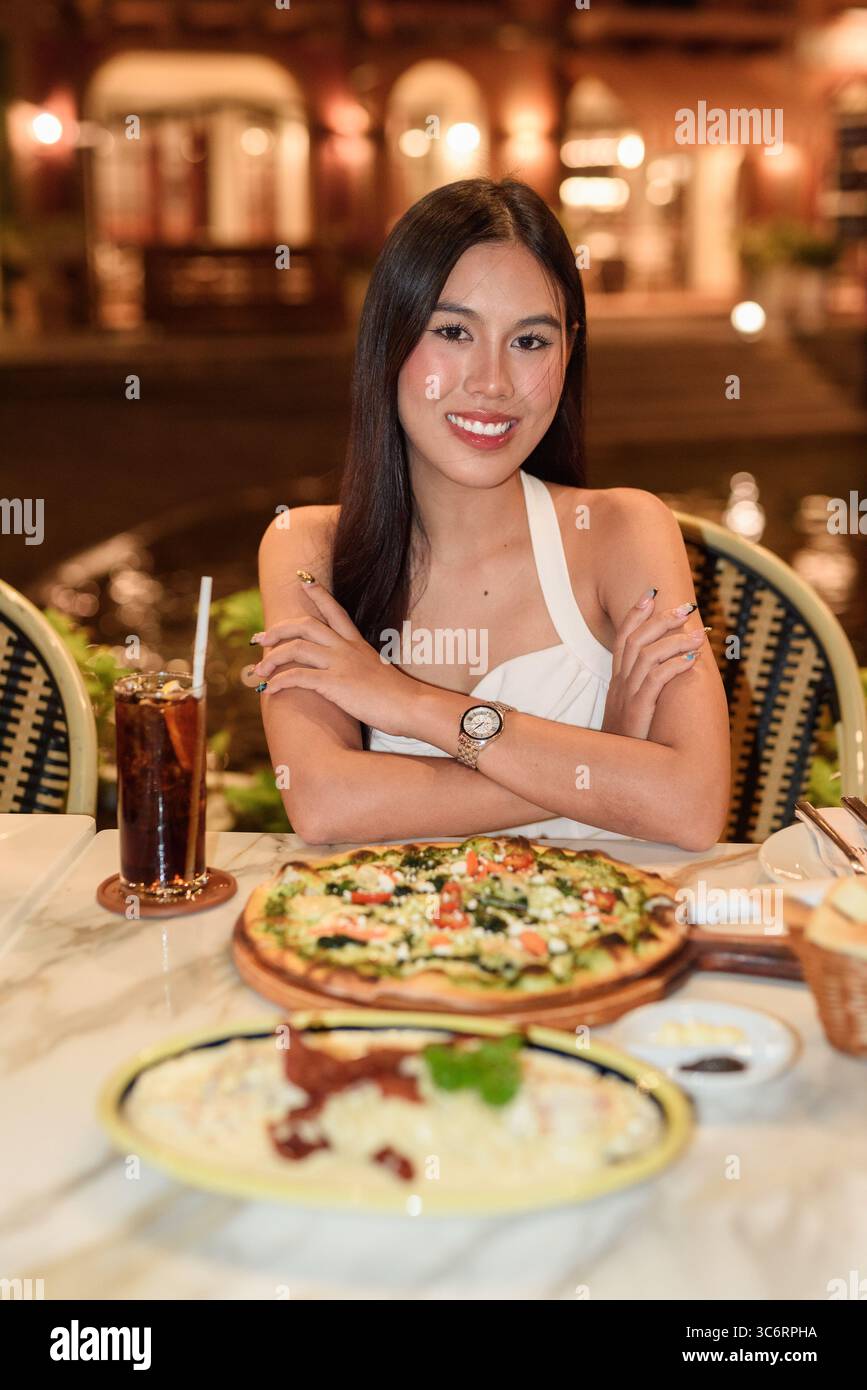Portrait d'une belle jeune femme asiatique avec de longs cheveux noirs dans la ville de style européen manger le dîner. Élégant touriste féminin en plein air, appréciant pittoresque Banque D'Images