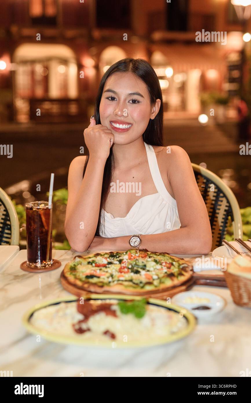 Portrait d'une belle jeune femme asiatique avec de longs cheveux noirs dans la ville de style européen manger le dîner. Élégant touriste féminin en plein air, appréciant pittoresque Banque D'Images
