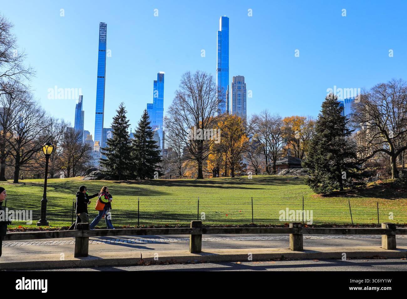 Vue des gens marchant à travers Central Park avec New York City et ciel bleu Banque D'Images