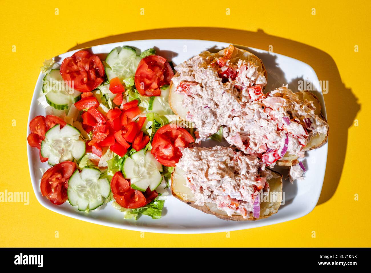 Une salade de thon en conserve servie dans une assiette. Le thon est servi sur une pomme de terre cuite au four avec une salade de feuilles vertes fraîches. Un repas soucieux de la santé Banque D'Images