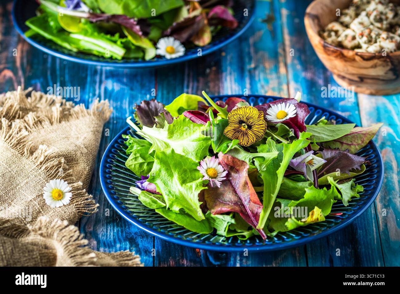 Salade fraîche avec des variétés mélangées et des fleurs comestibles sur un fond en bois bleu rustique Banque D'Images