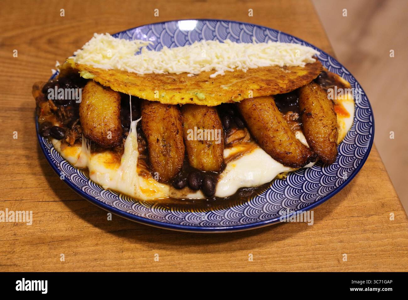 Cuisine vénézuélienne en Espagne. Crêpe de maïs Cachapa avec plantains (bananes de cuisson), haricots noirs, viande et fromage. Banque D'Images