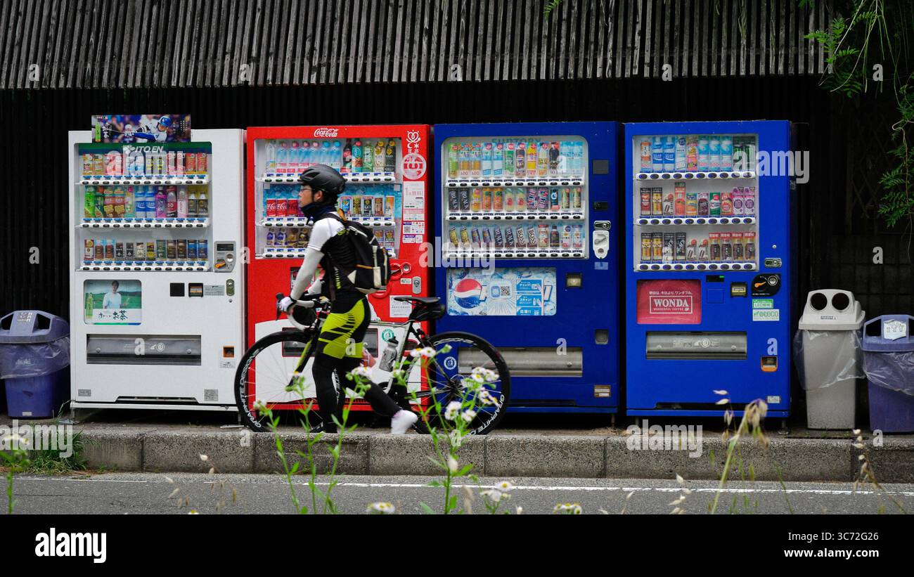 Cycliste passant devant des distributeurs automatiques japonais colorés à Kyoto, Japon. Scène de style de vie urbain avec boissons, technologie et routine quotidienne. Banque D'Images