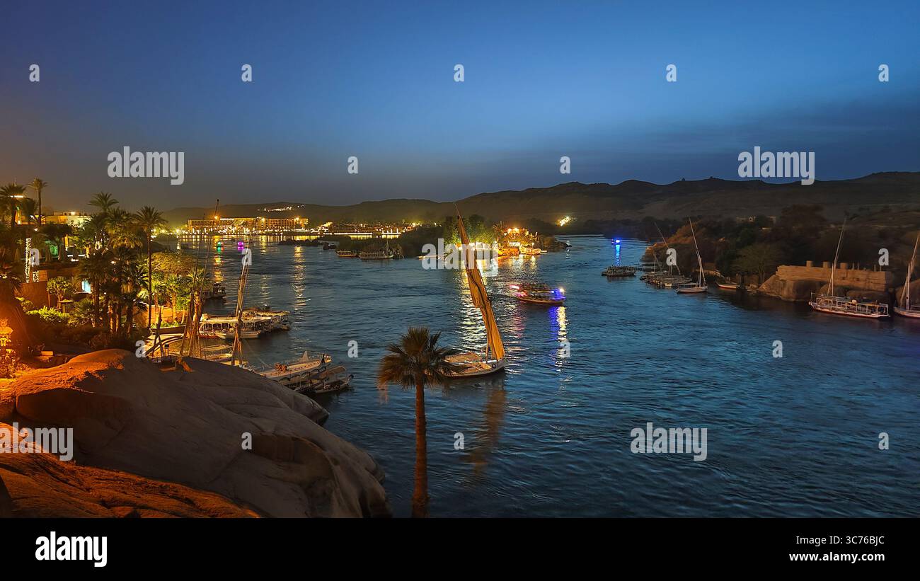 Felouques illuminées naviguant sur le nil la nuit, avec la ville d'Assouan en arrière-plan, Egypte Banque D'Images