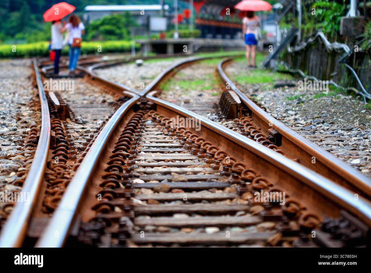 Des voies ferrées rouillées convergent à un point de commutation à Pingxi, New Taipei City, Taiwan, avec des figures floues tenant des parapluies rouges en arrière-plan, sugg Banque D'Images
