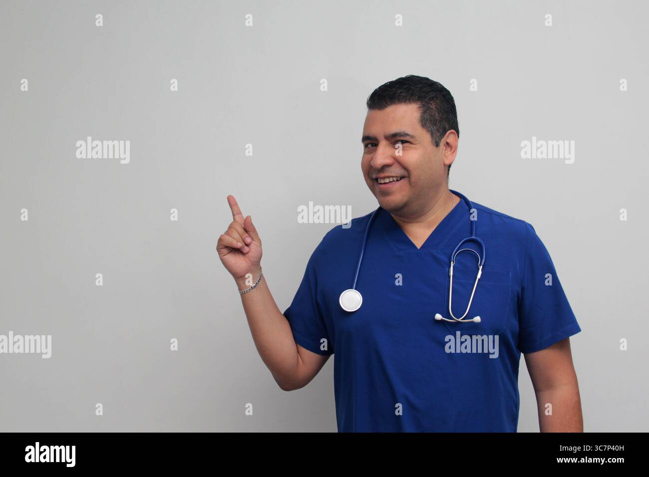 Médecin spécialiste latino-américain à la peau foncée avec un stéthoscope pointe avec son doigt avec une expression de joie et de surprise Banque D'Images Médecin spécialiste latino-américain à la peau foncée avec un stéthoscope pointe avec son doigt avec une expression de joie et de surprise Banque D'Images