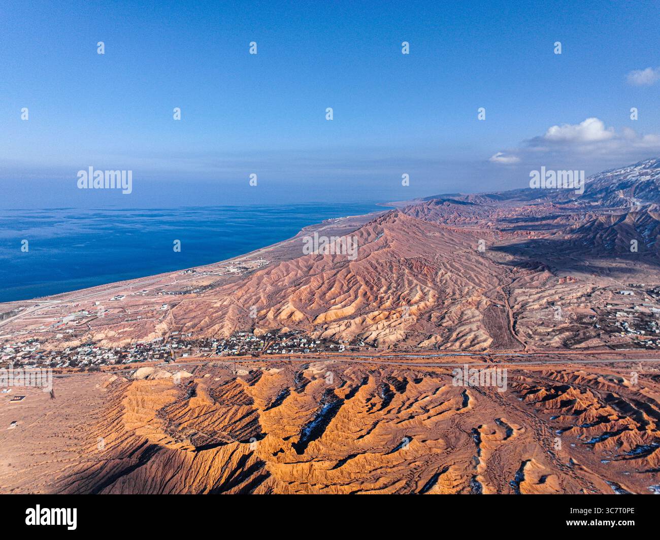Un plan aérien large capture les formations rouges et brunes de mars Canyon menant à une ville, avec le vaste lac bleu Issyk Kul qui s'étend jusqu'au Ho Banque D'Images