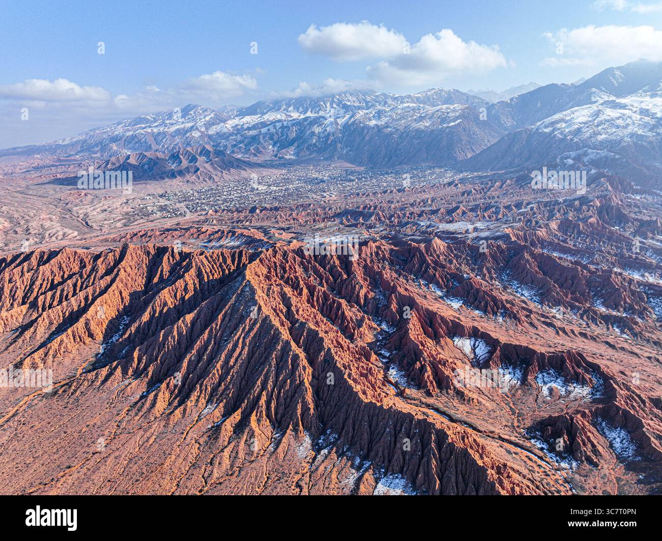 Un grand drone aérien capture le vaste paysage rouge de mars Canyon avec ses formations distinctives, une ville et des montagnes enneigées Banque D'Images