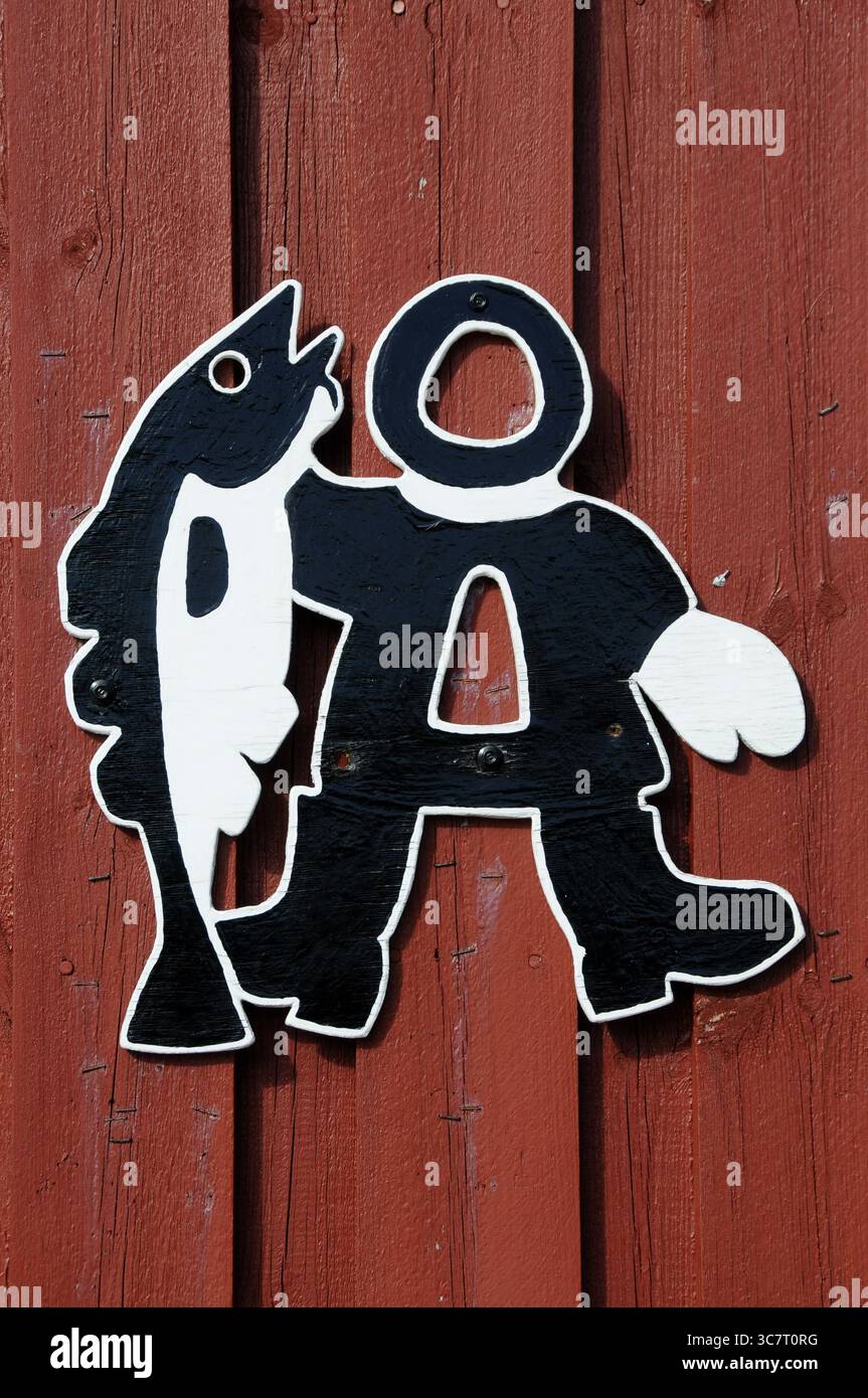 Figure stylisée en noir et blanc d'un pêcheur tenant un poisson sur un mur de bois à Lofoten, Norvège, août 2010. Banque D'Images