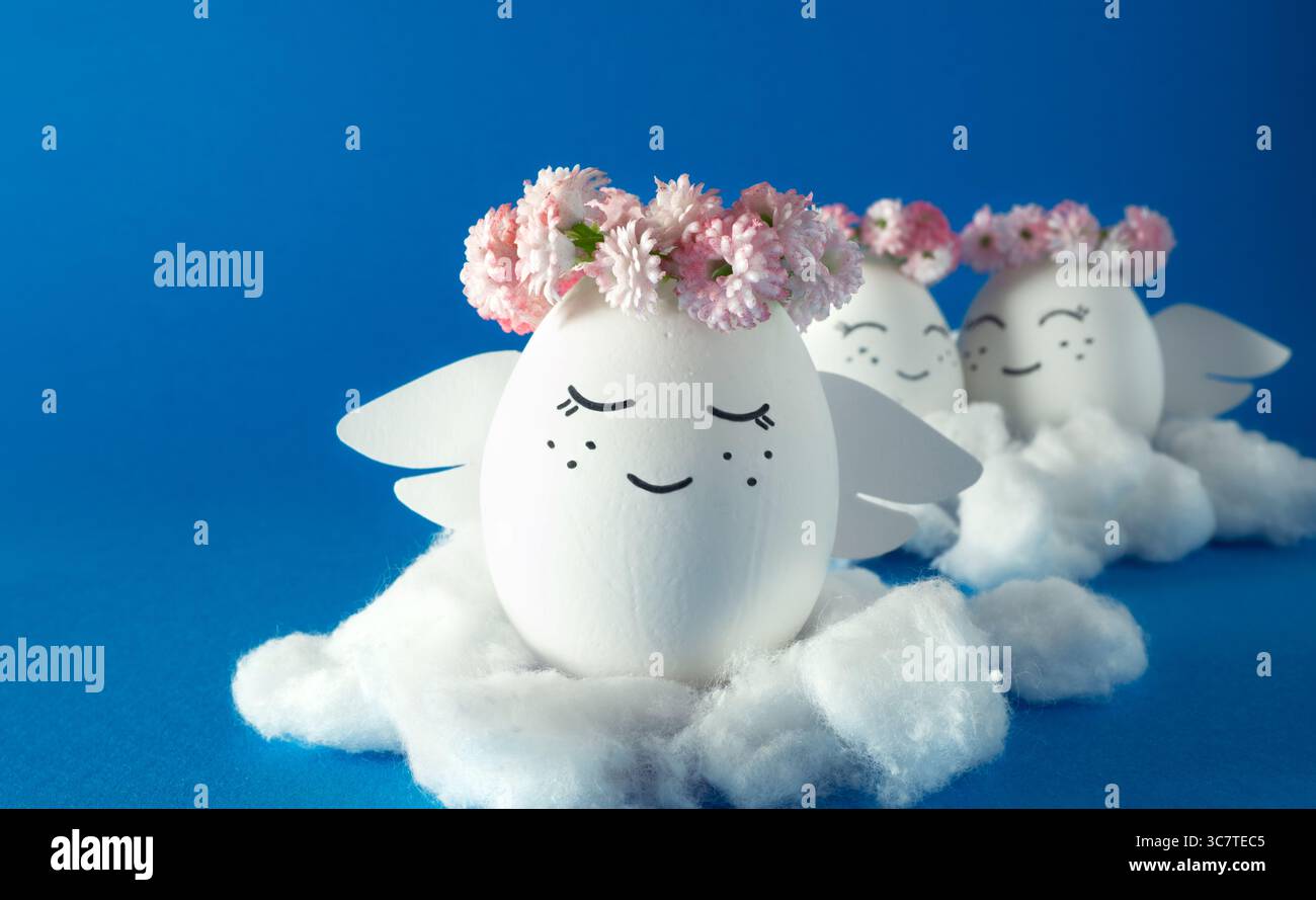 Anges faits d'oeufs dans des couronnes de fleurs sur les nuages. Œufs de Pâques décorés. Fond bleu. Banque D'Images