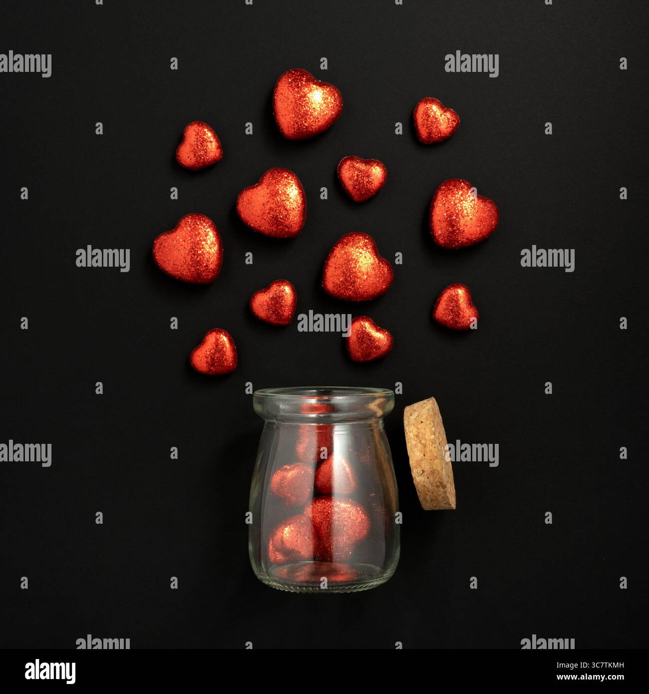 Cœurs brillants rouges qui volent hors d'un bocal en verre. Fond noir. Carte de Saint-Valentin Banque D'Images