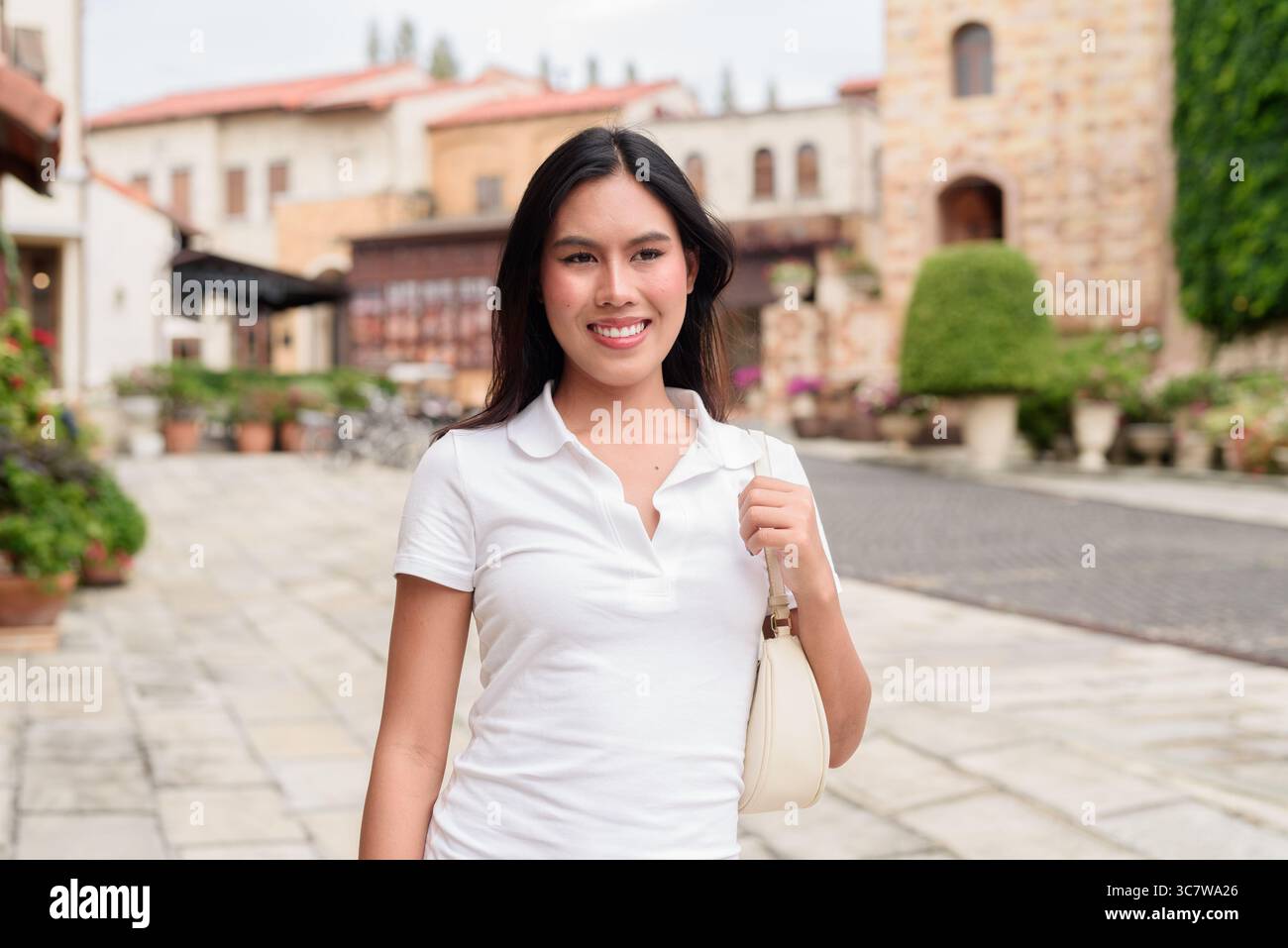 Belle jeune femme asiatique en polo marchant le long de la vieille rue de la ville de style européen. Portrait de voyage élégant entouré d'architecture, naturel ex Banque D'Images