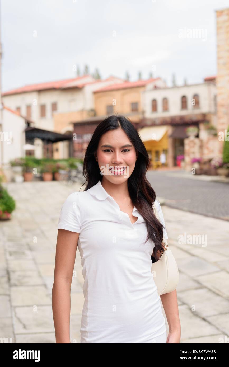 Belle jeune femme asiatique en polo marchant le long de la vieille rue de la ville de style européen. Portrait de voyage élégant entouré d'architecture, naturel ex Banque D'Images