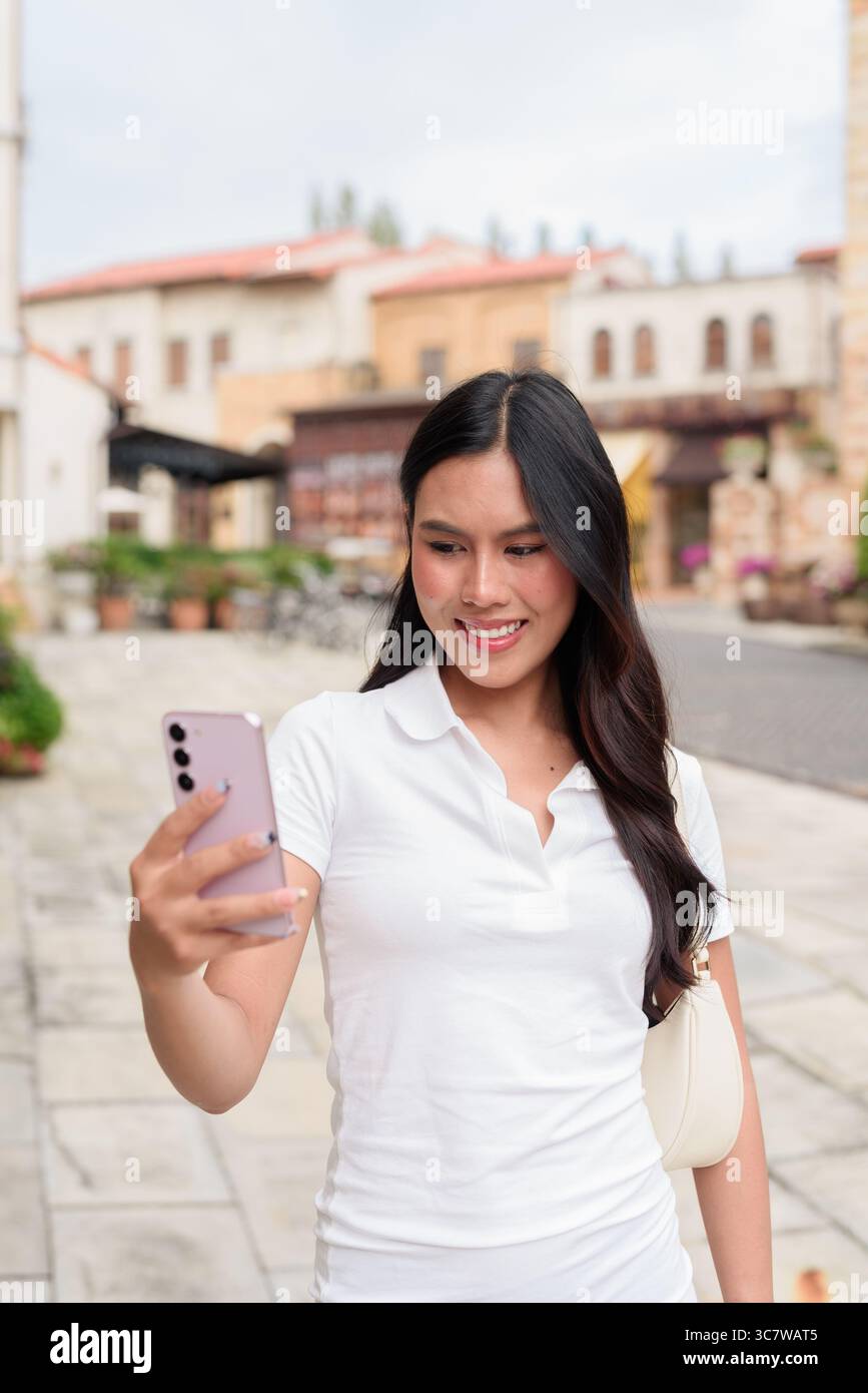 Belle jeune femme asiatique en polo marchant le long de la vieille rue de la ville de style européen. Portrait de voyage élégant entouré d'architecture, naturel ex Banque D'Images