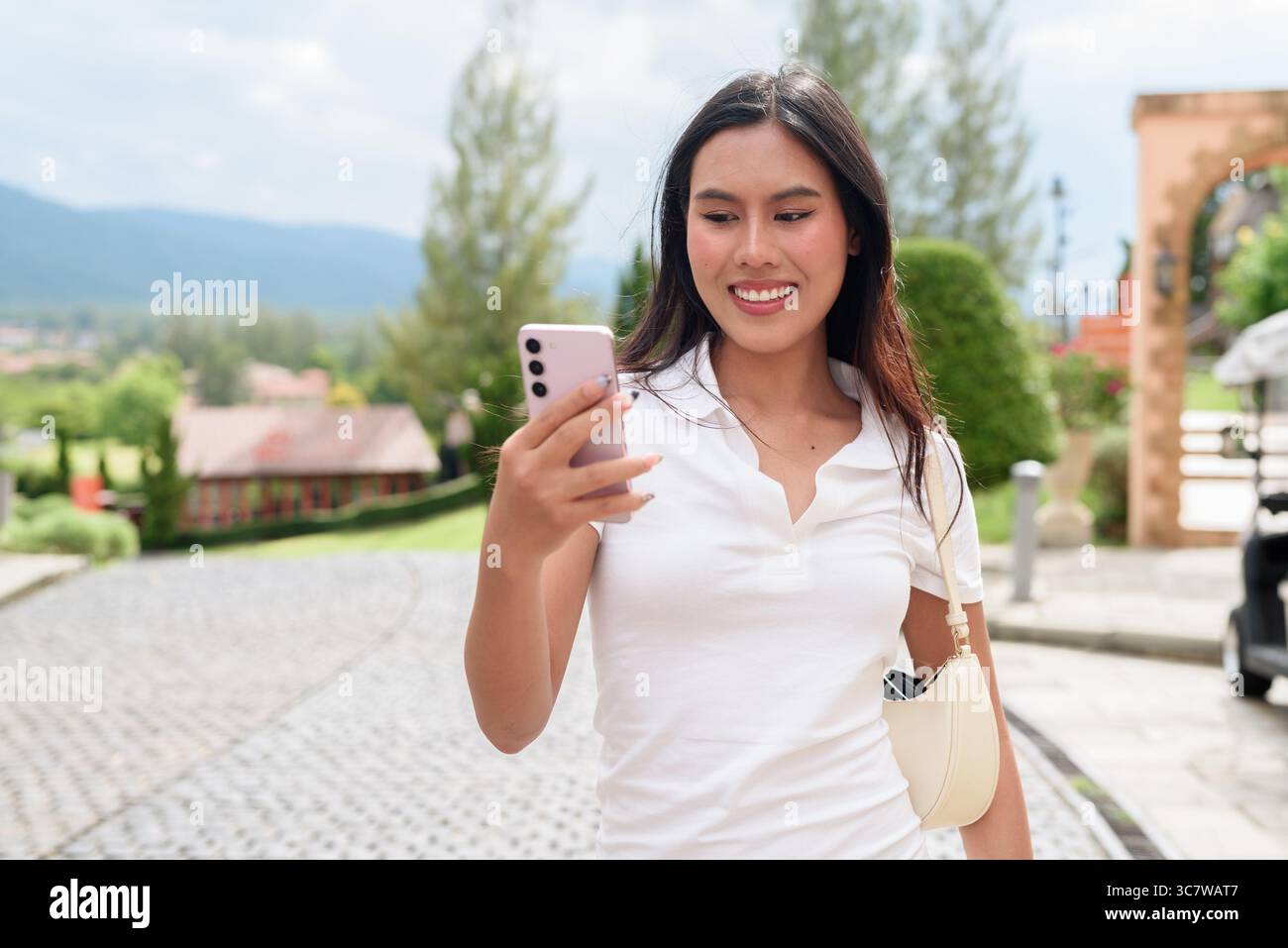Belle jeune femme asiatique en polo marchant le long de la vieille rue de la ville de style européen. Portrait de voyage élégant entouré d'architecture, naturel ex Banque D'Images