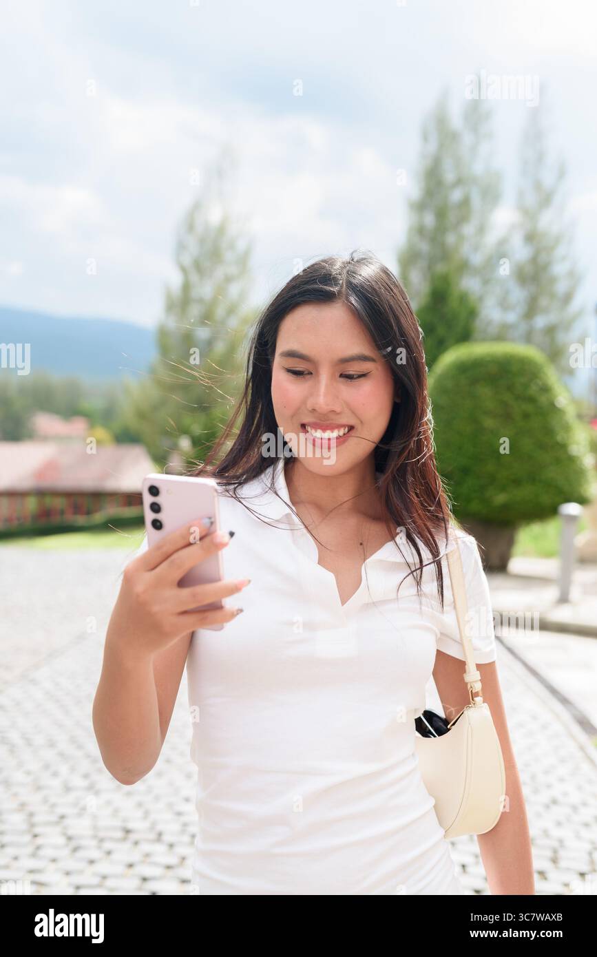 Belle jeune femme asiatique en polo marchant le long de la vieille rue de la ville de style européen. Portrait de voyage élégant entouré d'architecture, naturel ex Banque D'Images