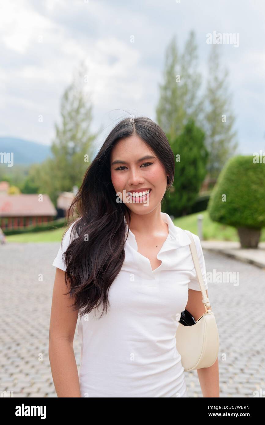 Belle jeune femme asiatique en polo marchant le long de la vieille rue de la ville de style européen. Portrait de voyage élégant entouré d'architecture, naturel ex Banque D'Images