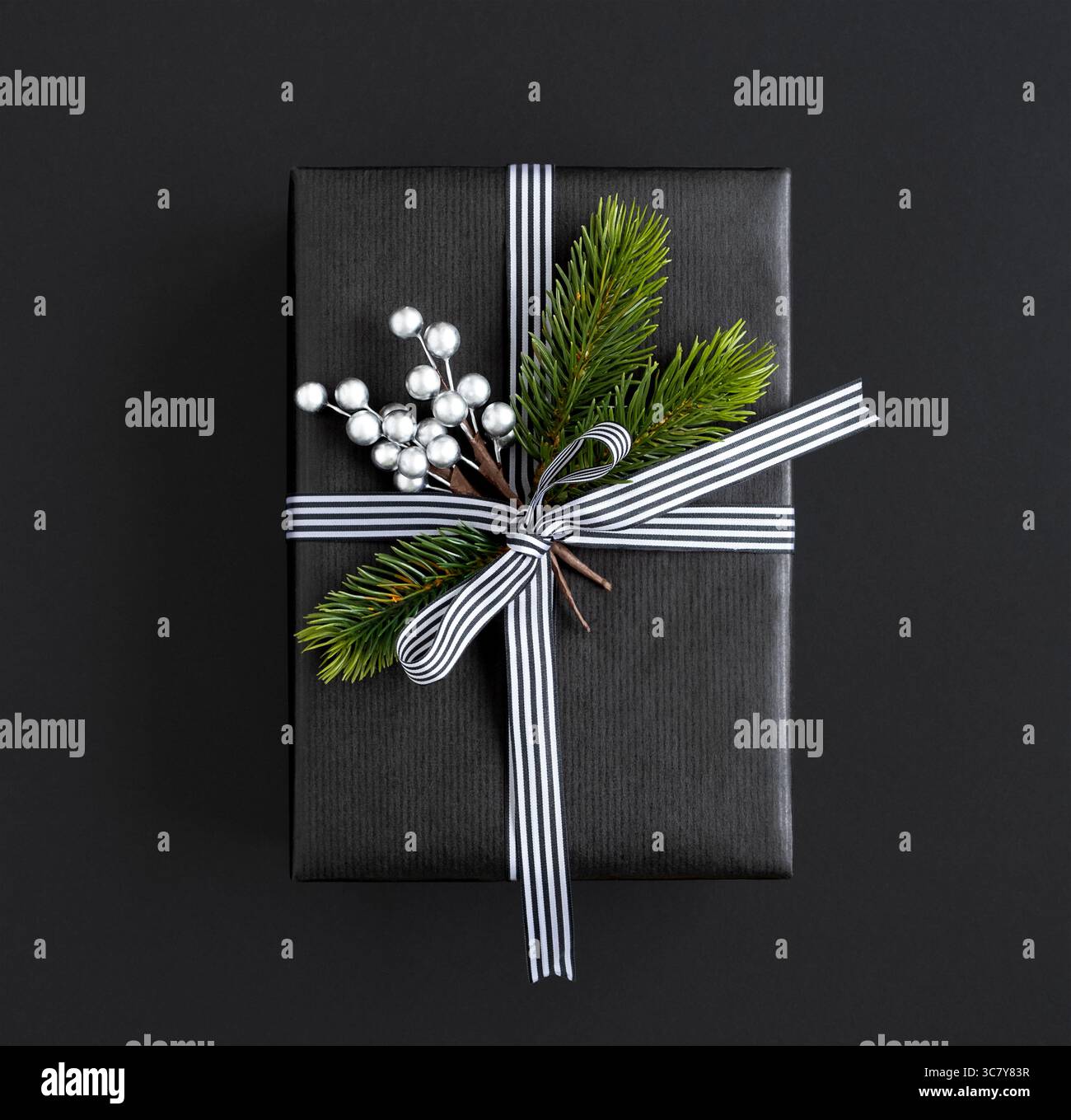 Boîte cadeau noire avec ruban, branches d'épicéa et baies argentées sur fond sombre Banque D'Images