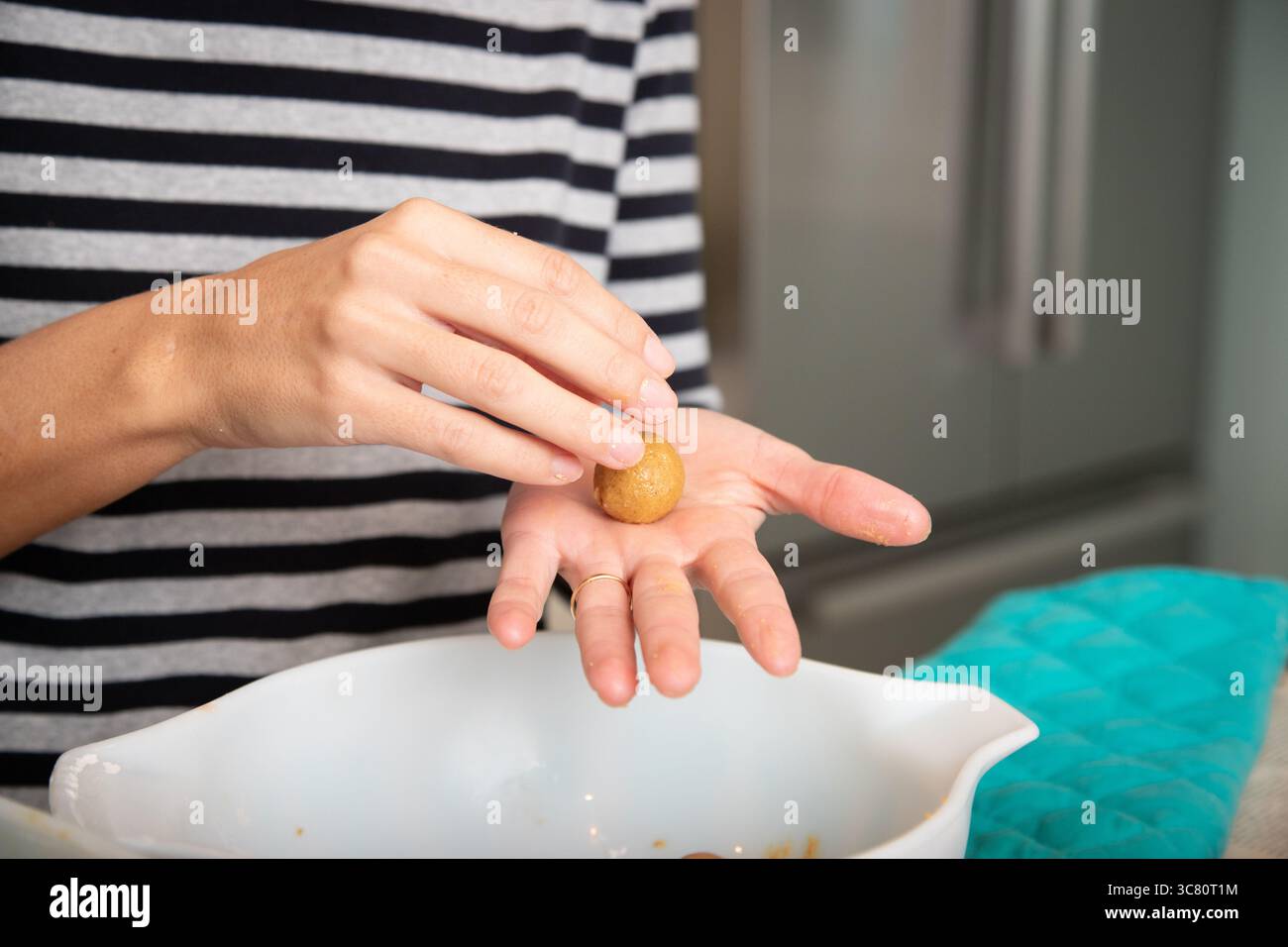 Gros plan d'une femme adulte moyenne debout dans une cuisine roulant des boules de pâte à biscuits dans sa main Banque D'Images