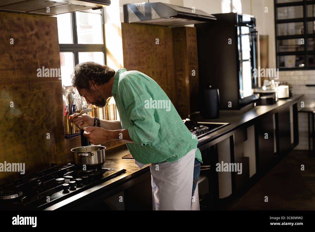 Pot en acier inoxydable mijotant sur la table de cuisson à gaz dans la cuisine avec dosseret, ustensiles et lumière de fenêtre Banque D'Images