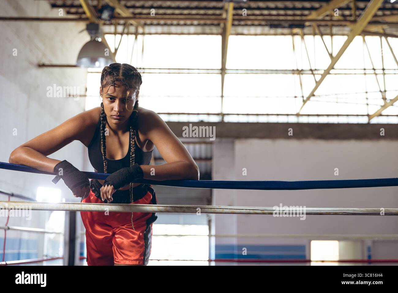 Boxeur afro-américain portant soutien-gorge de sport formation dans l'anneau de gymnastique de boxe penché sur la corde Banque D'Images