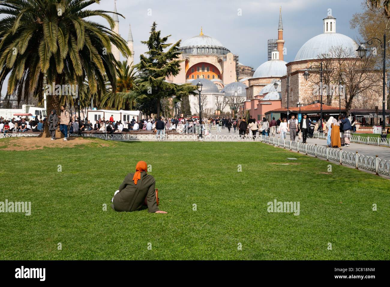 Une femme portant un hijab est assise sur l'herbe devant la basilique Sainte-Sophie à Istanbul, en Turquie, tandis que d'autres touristes se promènent et profitent de la journée. Banque D'Images Une femme portant un hijab est assise sur l'herbe devant la basilique Sainte-Sophie à Istanbul, en Turquie, tandis que d'autres touristes se promènent et profitent de la journée. Banque D'Images