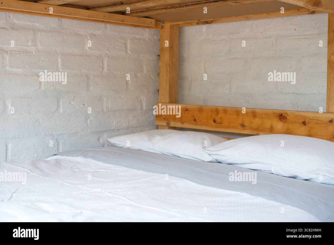 Lit superposé inférieur avec draps blancs et oreillers, créant une atmosphère simple mais accueillante dans une chambre d'auberge avec murs de briques peints en blanc et Banque D'Images