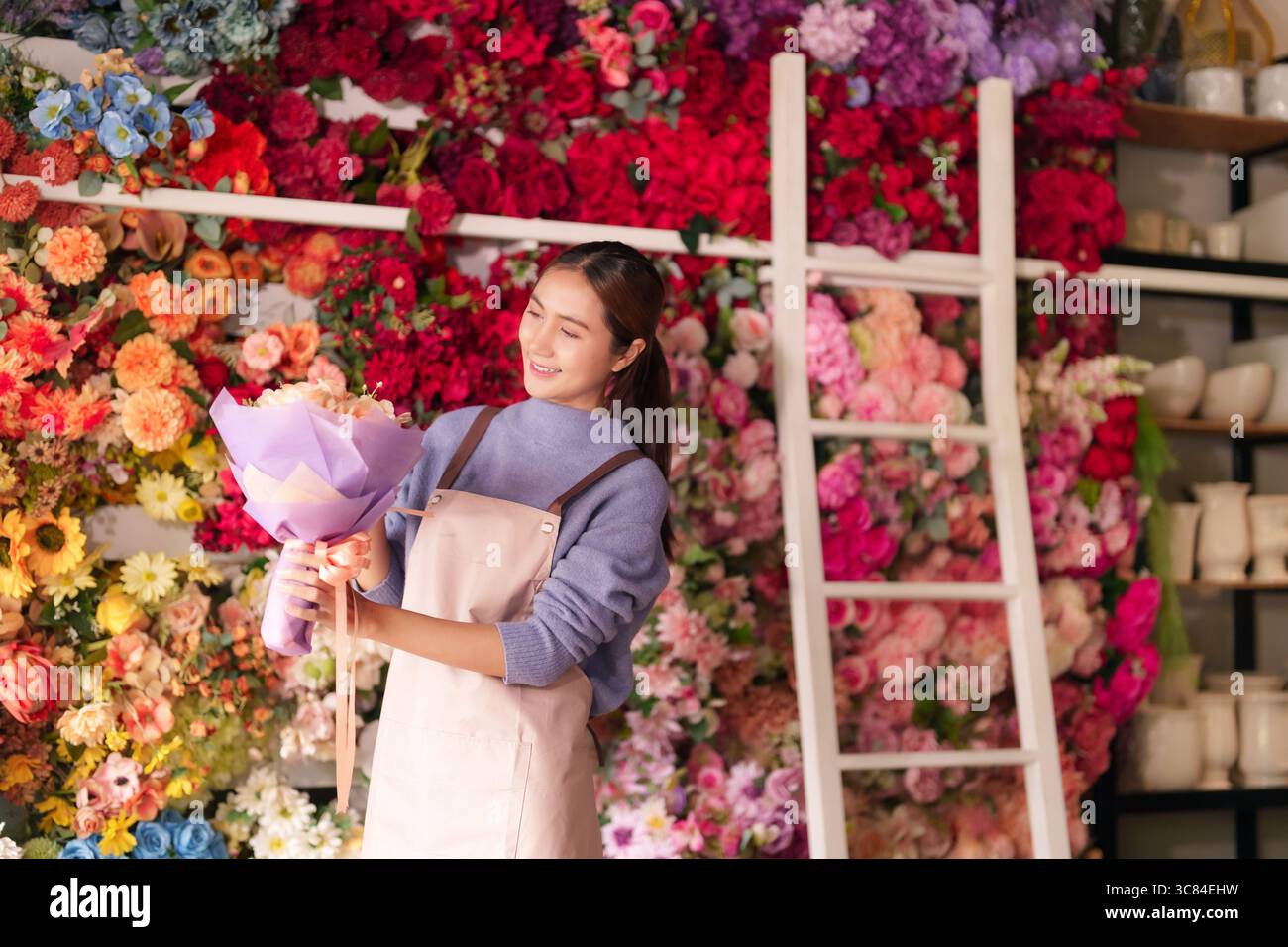 Fleuriste professionnel asiatique adulte prépare de belles fleurs colorées. Femme joyeuse travaille dans un magasin floral animé créant des arrangements exquis pour cl Banque D'Images
