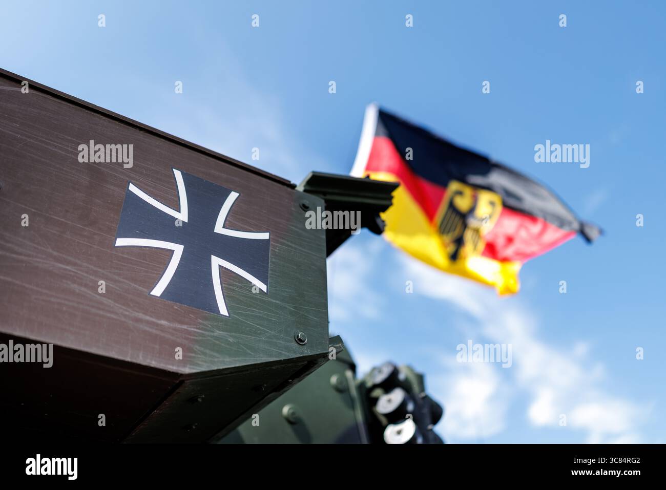 01 août 2025, Bavière, Grafenwöhr : le logo de la Bundeswehr de la République fédérale d'Allemagne, la croix de fer, peut être vu sur un char militaire peint en vert à Grafenwoehr (Bavière) le 01.08.2025. L'emblème est un emblème national et un symbole de bravoure, d'amour de la liberté et de chevalerie. Les forces armées de la Bundeswehr se composent des quatre branches Armée, Armée de l'Air, Marine et Cyber and information Space ainsi que du secteur de soutien. En arrière-plan, le drapeau allemand avec les armoiries allemandes vole contre un ciel bleu. (Image symbole, photo symbole, illustration, photo symbolique, photo illustrative, Banque D'Images