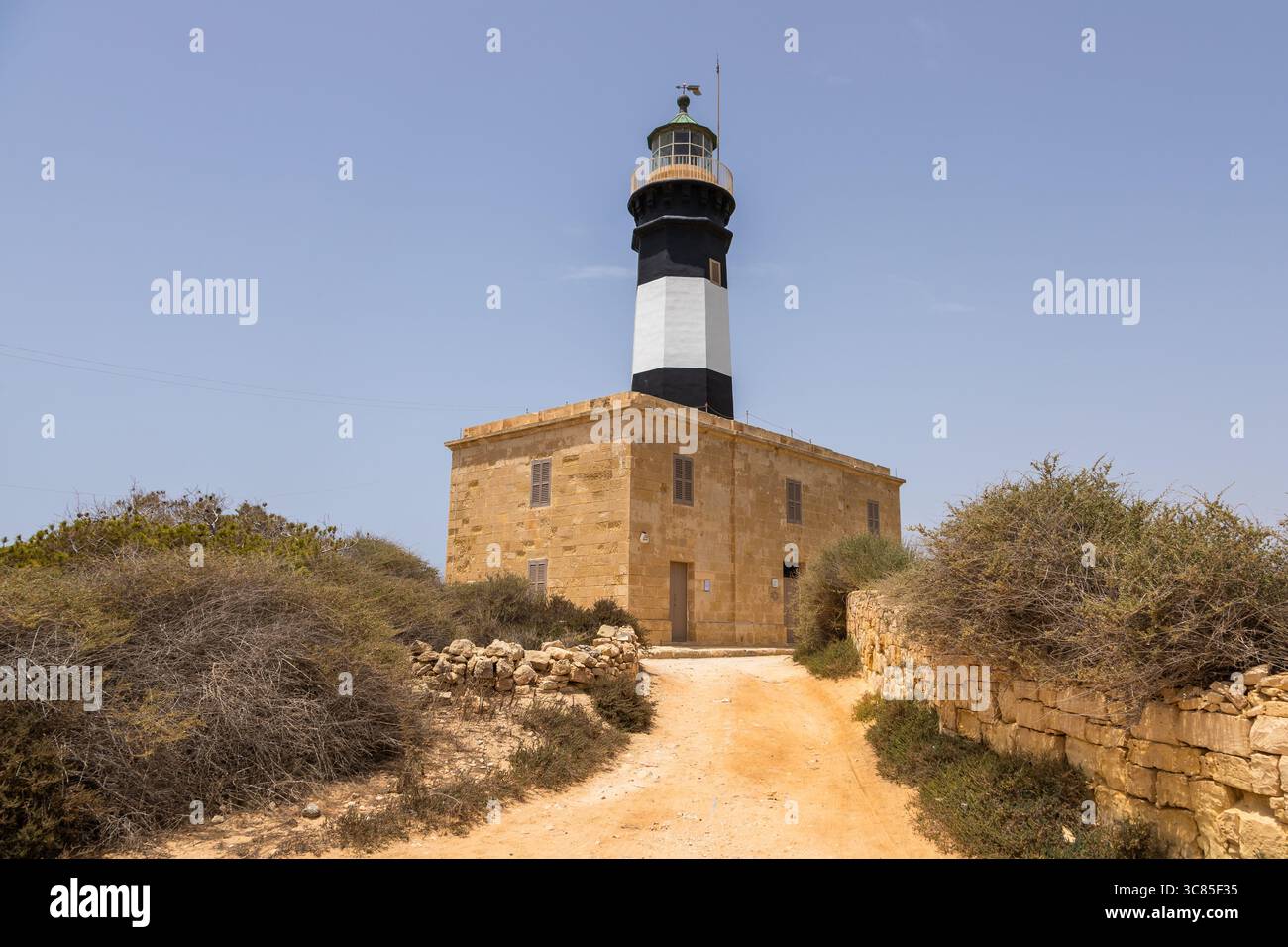Phare historique avec des rayures noires et blanches à Fort Delimara à Malte entouré par un paysage méditerranéen sec. Banque D'Images