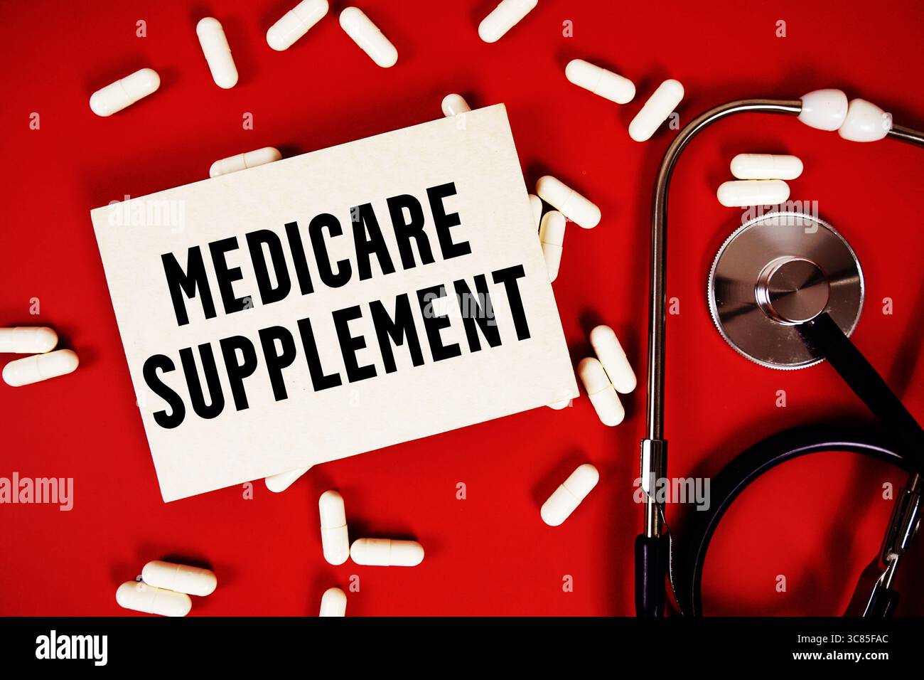 Texte du supplément Medicare écrit sur une carte papier avec stéthoscope et capsule de médicament sur fond rouge Banque D'Images