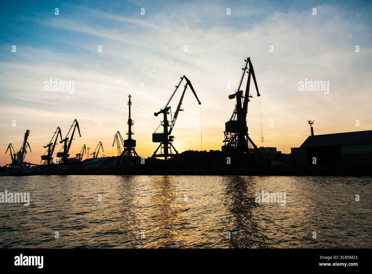 Silhouettes de grues dans le port au coucher du soleil. Banque D'Images