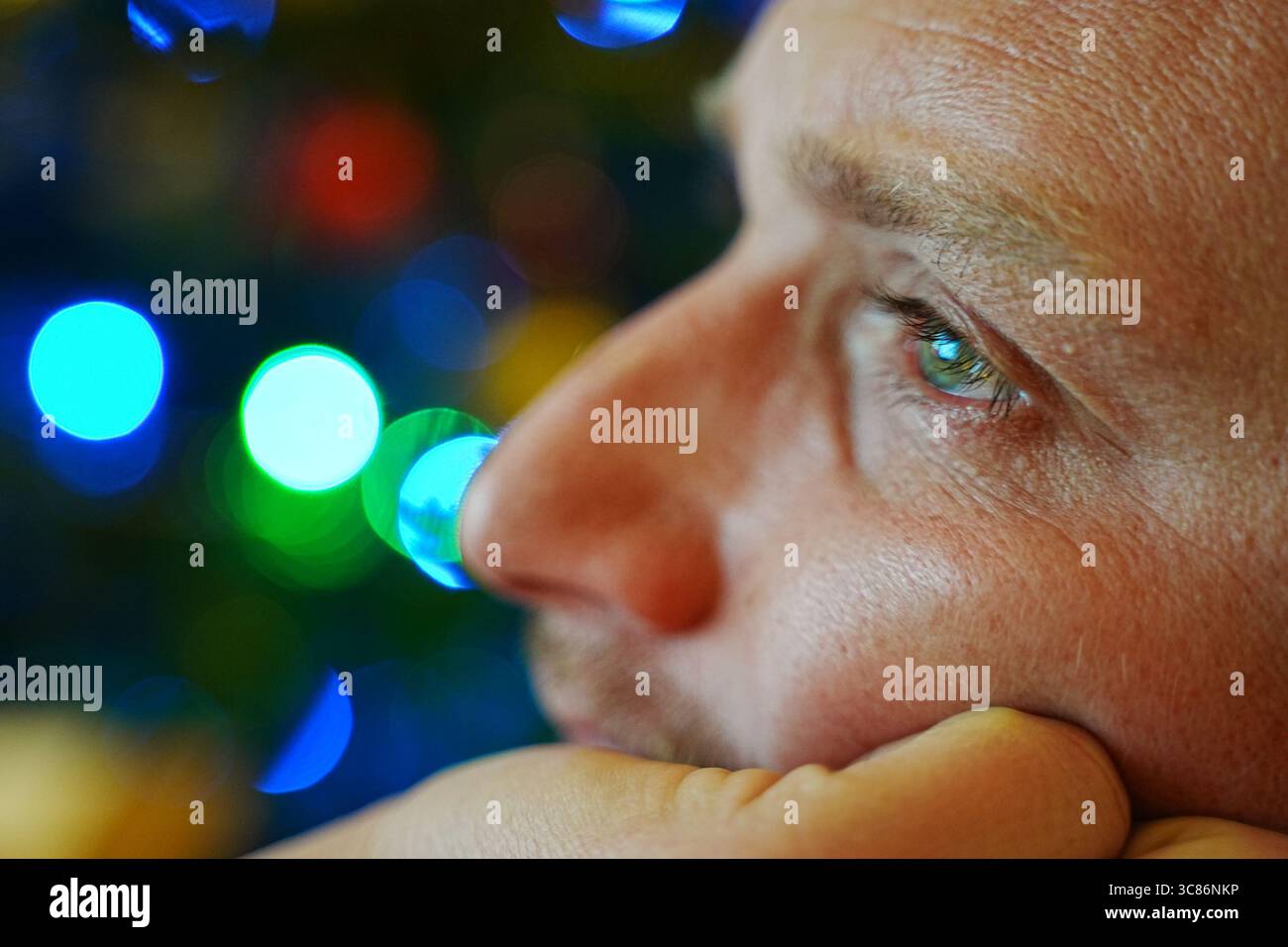 Noël. Gros plan d'une personne regardant soigneusement au loin sur fond de lumières bokeh vibrantes. L'image capture un moment pensif, Banque D'Images