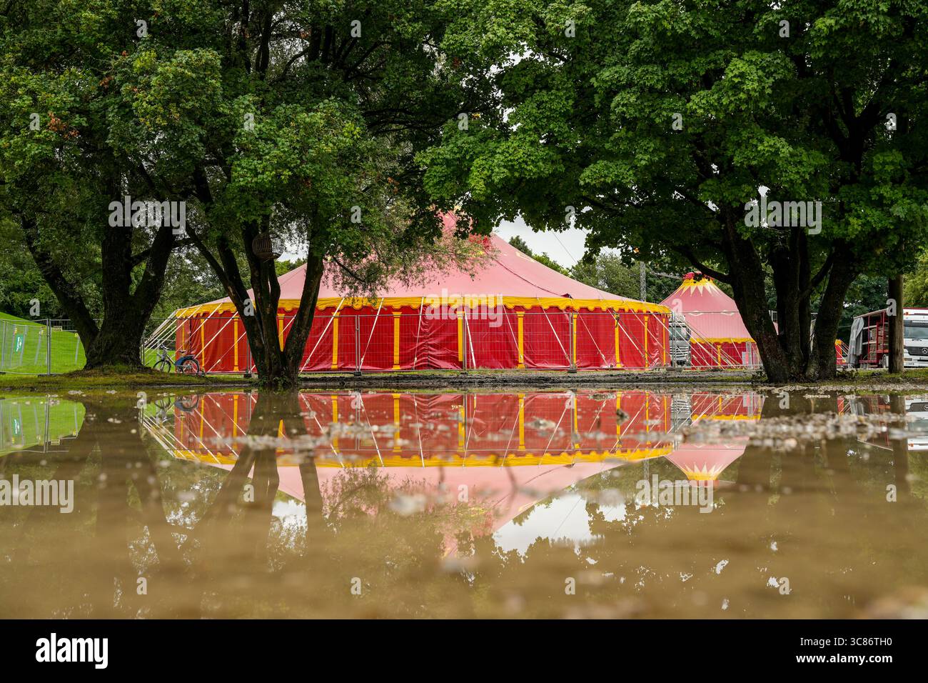 Grande tente de cirque rouge au milieu d'Une inondation en raison de fortes pluies ou de fortes eaux. L'eau reflète la tente et les arbres environnants Banque D'Images