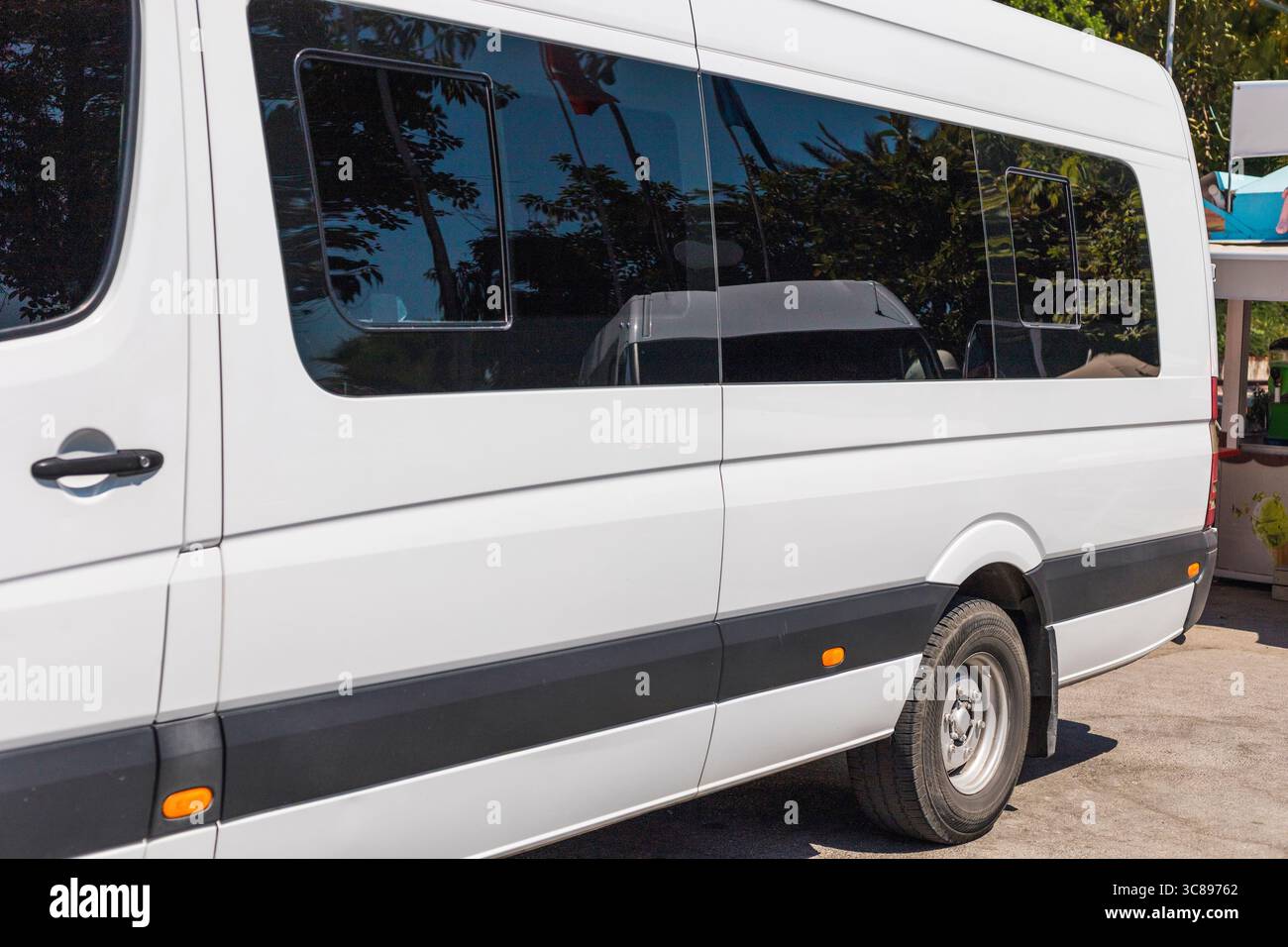 Une fourgonnette blanche est garée sous le soleil, montrant son design élégant et ses fenêtres teintées, avec des palmiers offrant une toile de fond tropicale. Le véhicule Banque D'Images