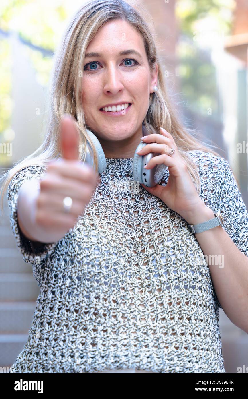 Femme heureuse donnant les pouces vers le haut, tenant le smartphone, geste positif, souriant à l'extérieur Banque D'Images