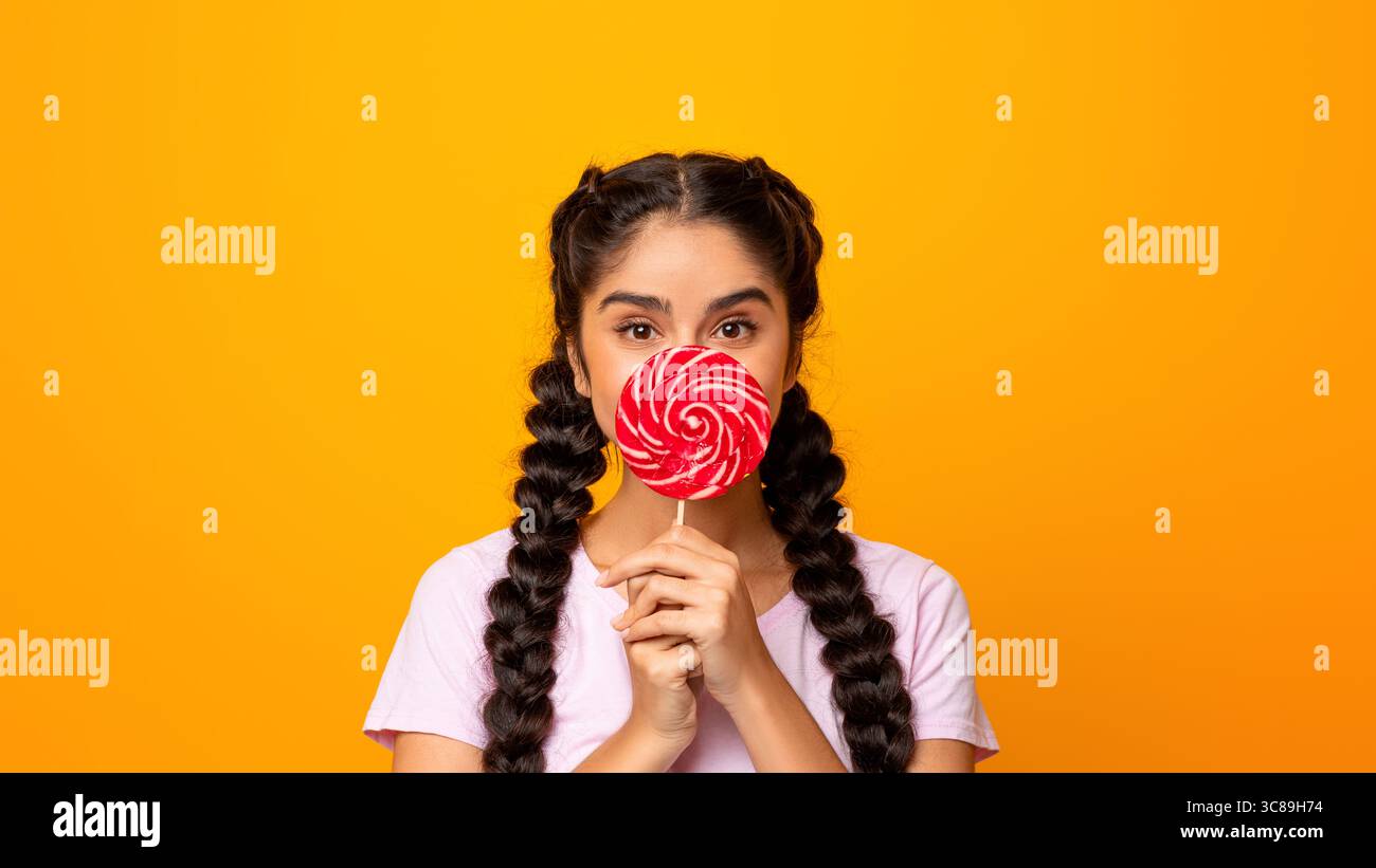 Femme indienne tenant une lollipop, couvrant la bouche avec des bonbons Banque D'Images