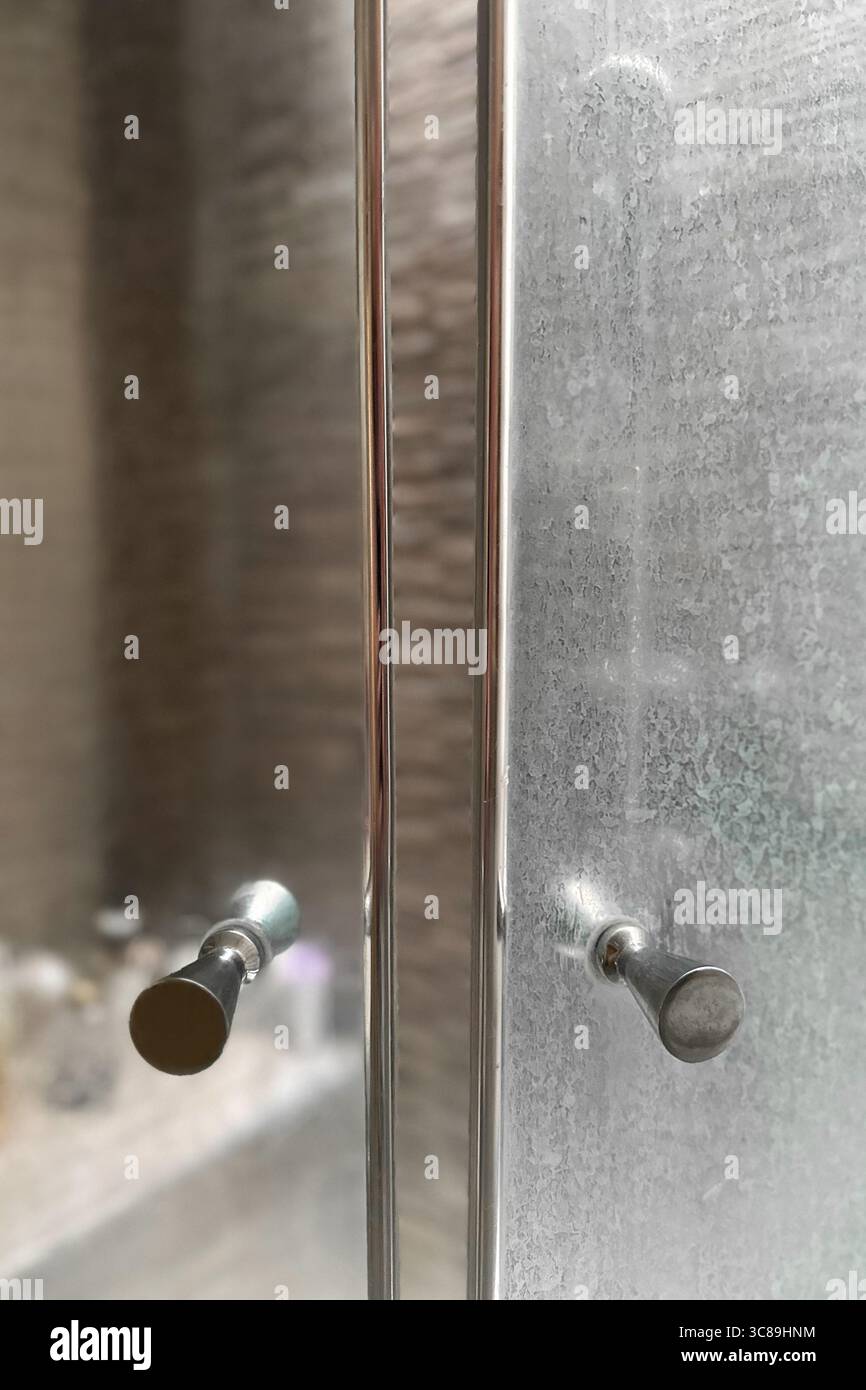 Gros plan d'une porte en verre de douche sale avec des résidus minéraux blancs de l'eau dure et de l'écume de savon.un autre côté de la porte après le nettoyage. Banque D'Images