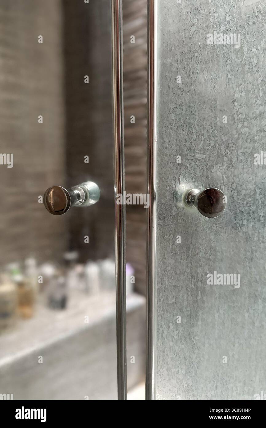 Gros plan d'une porte en verre de douche sale avec des résidus minéraux blancs de l'eau dure et de l'écume de savon.un autre côté de la porte après le nettoyage. Banque D'Images