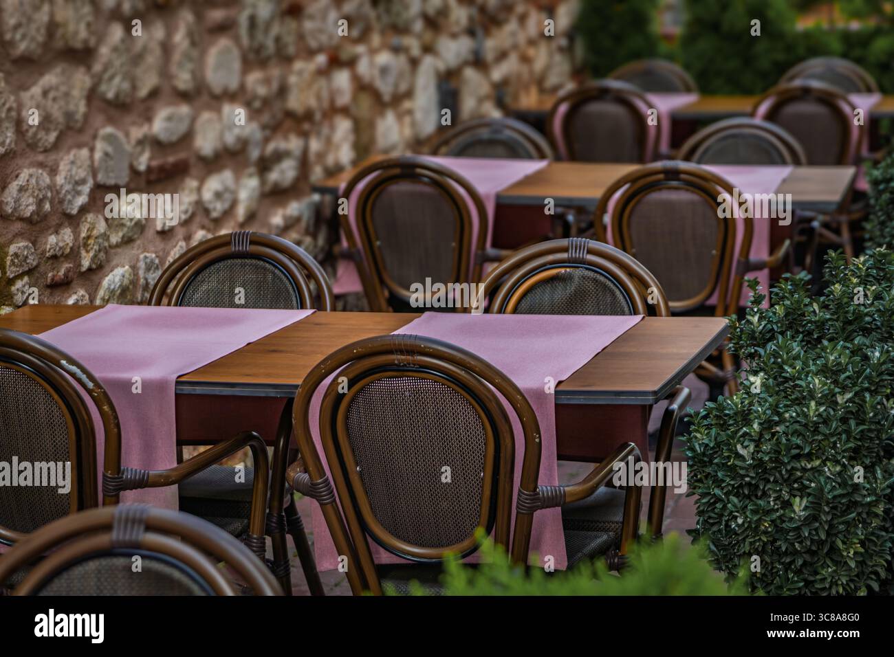 Des tables à manger en plein air avec des coureurs roses et des chaises tissées sont installées contre un mur de pierre rustique dans un café de rue calme à Istanbul, en Turquie Banque D'Images