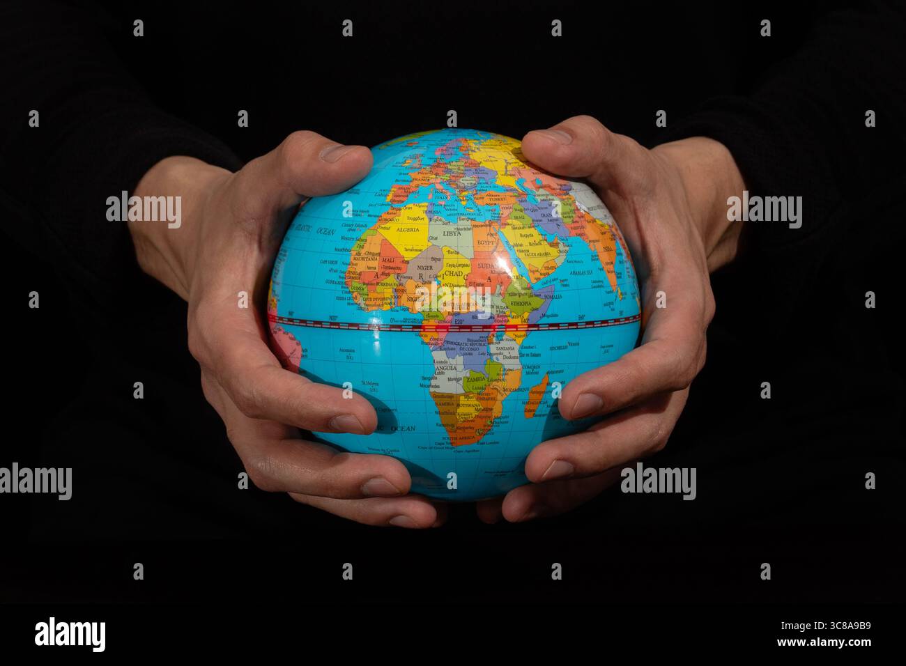 Gros plan sur une main masculine tenant un globe terrestre avec un continent africain et un fond noir Banque D'Images