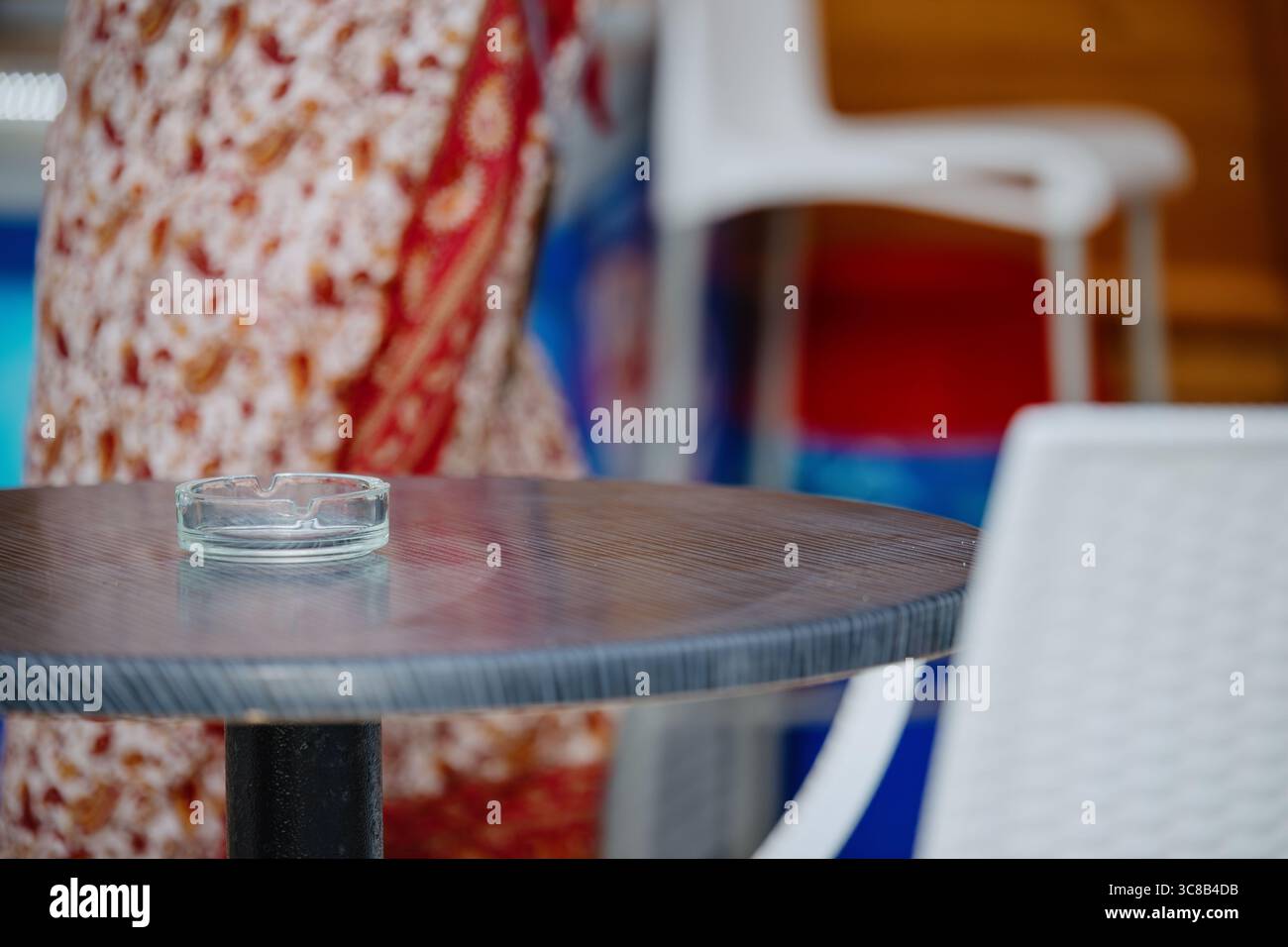 Une table avec un cendrier en verre près d'un bar de plage sur le bord de mer. En arrière-plan, une silhouette floue d'une femme dans une robe à motifs lumineux passant Banque D'Images