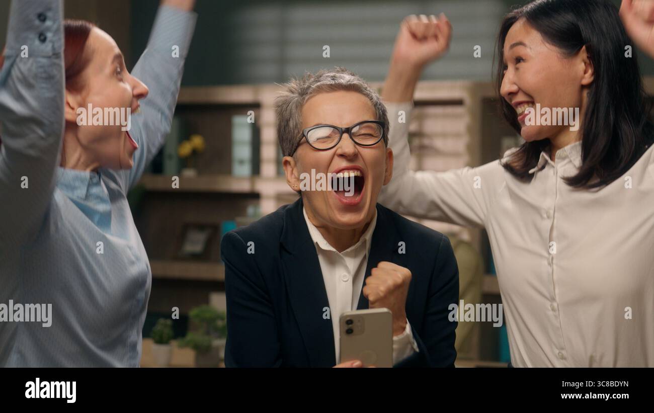 Heureux femmes excitées collègues groupe d'équipe tenant téléphone mobile multinationale lire de bonnes nouvelles femmes d'affaires gagnant la finance en ligne célébrant le bureau Banque D'Images