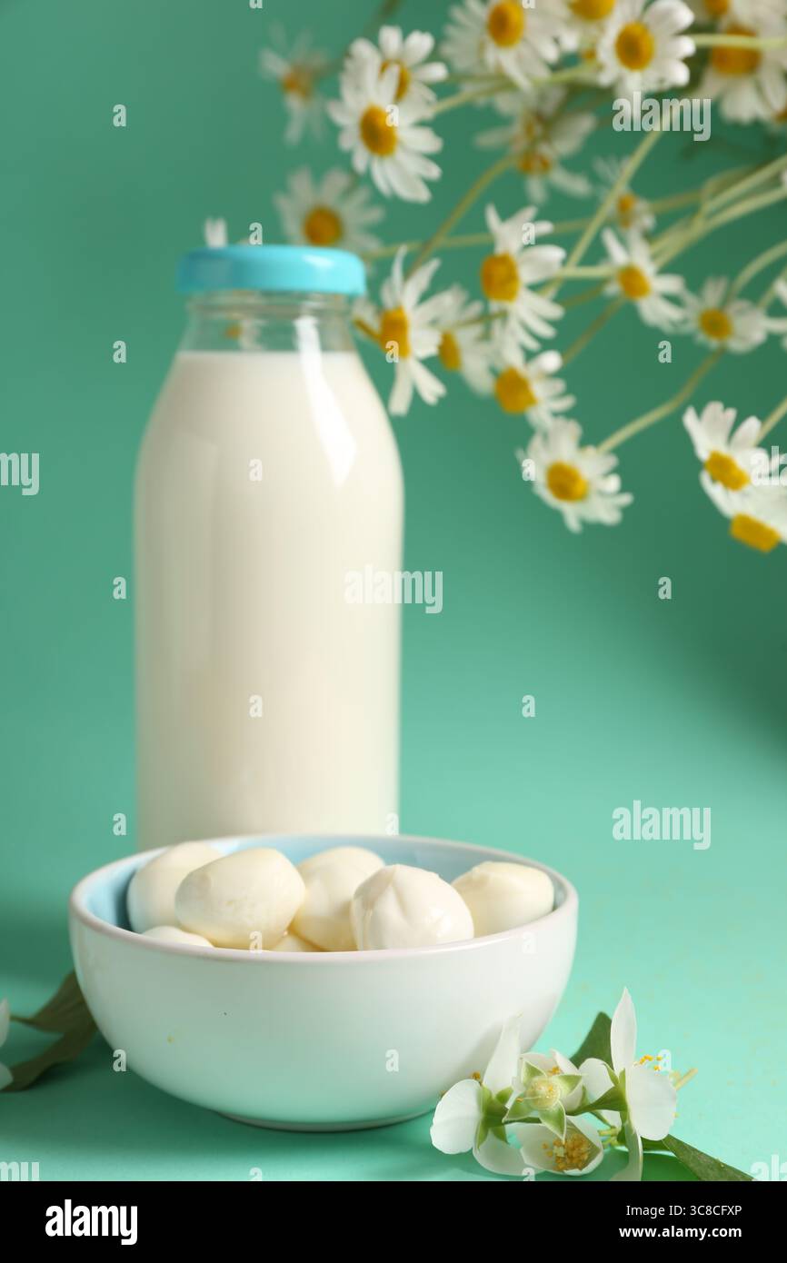 Lait frais en bouteille en verre, boules de mozzarella et fleurs sur fond turquoise, gros plan. Produits laitiers Banque D'Images