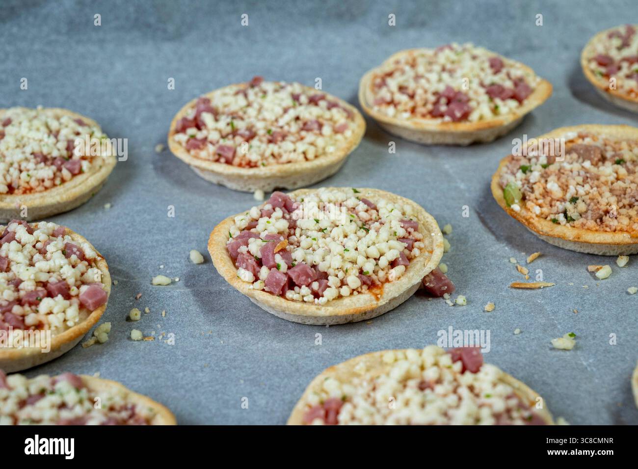Un plateau de mini pizzas avec garnitures de fromage et de jambon. Les pizzas sont disposées en rangée sur un comptoir Banque D'Images