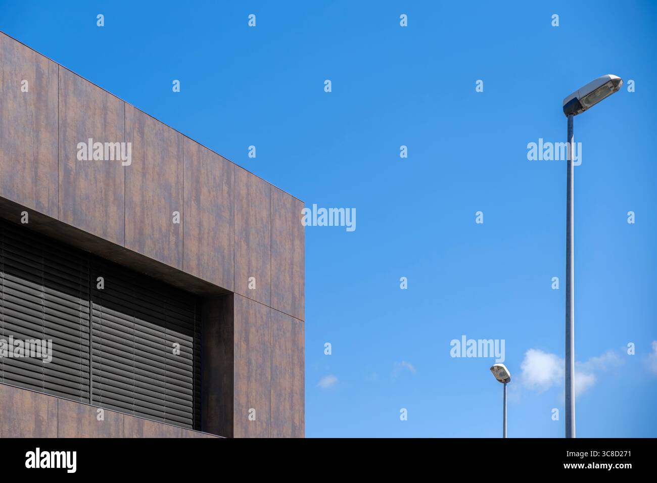 Façade de bâtiment contemporaine avec revêtement sombre et lampadaires contre ciel bleu clair. Architecture moderne, design urbain, formes géométriques Banque D'Images