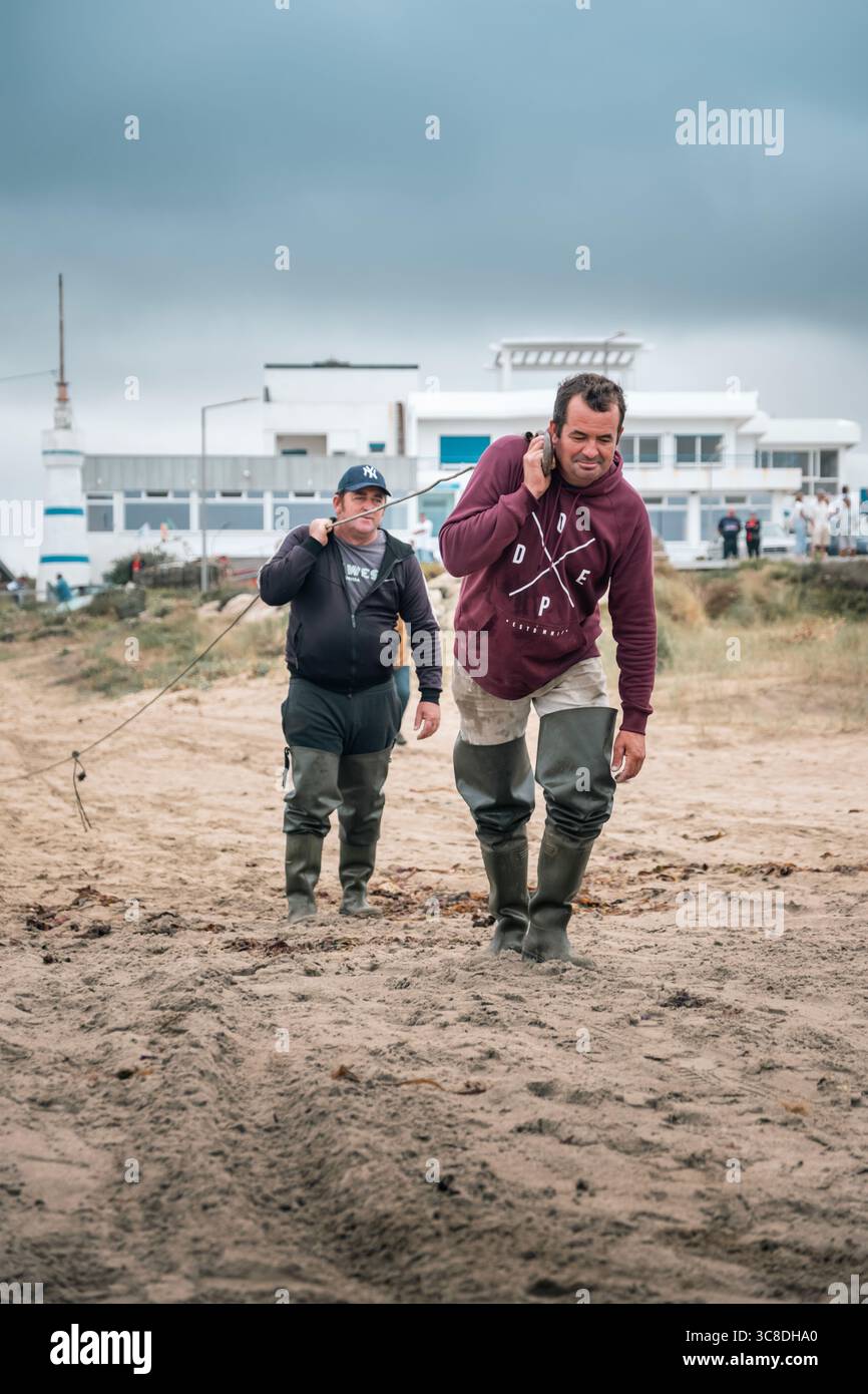 Pêcheurs portant corde pour transporter un bateau traditionnel à terre sur la plage portugaise. Région du Minho, travail côtier, travail maritime, vie de plage, industrie de la pêche Banque D'Images